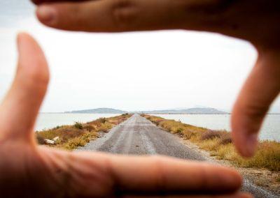 Blick durch mit Fingern gerahmten Ausschnitt auf eine lange Straße Richtung Horizont