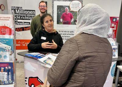 Ein junger Mann sitzt an einem Holztisch und hält ein Tablet in den Händen. Auf dem Bildschirm ist eine bunte Lern-App mit spielerischen Grafiken zu sehen, die Abkürzungen von Flughäfen anzeigen.