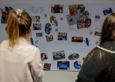 Zwei Personen betrachten eine Wand mit Fotos, Texten und QR-Codes aus dem Projekt #ABCforJobs.