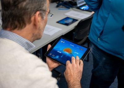 Eine Person hält ein Tablet und testet eine digitale Lernanwendung mit einem Sonnensymbol auf dem Bildschirm.