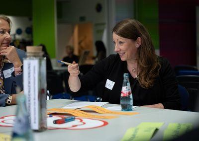 Zwei Personen betrachten eine Wand mit Fotos, Texten und QR-Codes aus dem Projekt #ABCforJobs.