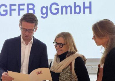 Überreichung der BNE-Zertifizierung an Frau Barbara Wagner. Man sieht insgesamt drei Personen, die auf das Zertifikat schauen und sich freuen.