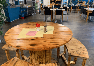 Großer runder Holztisch mit Sitzbänken im offenen Innenbereich des World Cafés.